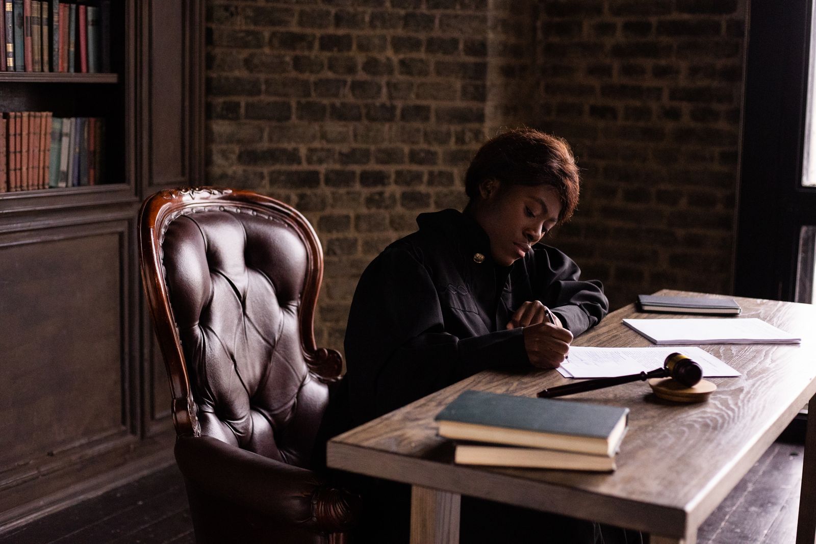 An advocate writing at a desk in chambers, law reports and a gavel beside her.